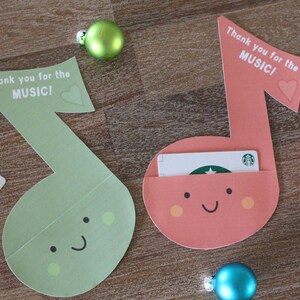 May include: Two green and pink musical note shaped cards with a happy face and a pocket for a gift card. The cards say "Thank you for the MUSIC!" with a heart.