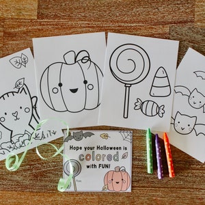 May include: Four black and white coloring pages featuring a pumpkin, a lollipop, a candy cane, bats, and a cat. The pages are on a wooden surface with green and purple crayons.
