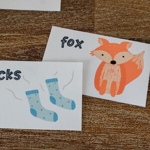 May include: Two white cards with illustrations and text. The first card has a blue sock with white polka dots and the word "socks". The second card has a fox with an orange body and the word "fox".