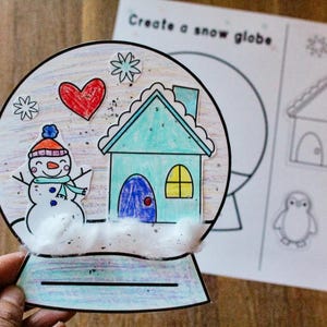 Puede incluir: Una manualidad de globo de nieve colorida y dibujada a mano. El globo presenta un muñeco de nieve, una casa, copos de nieve y un corazón rojo. El texto "Create a snow globe" es visible en la página. La manualidad es para niños.