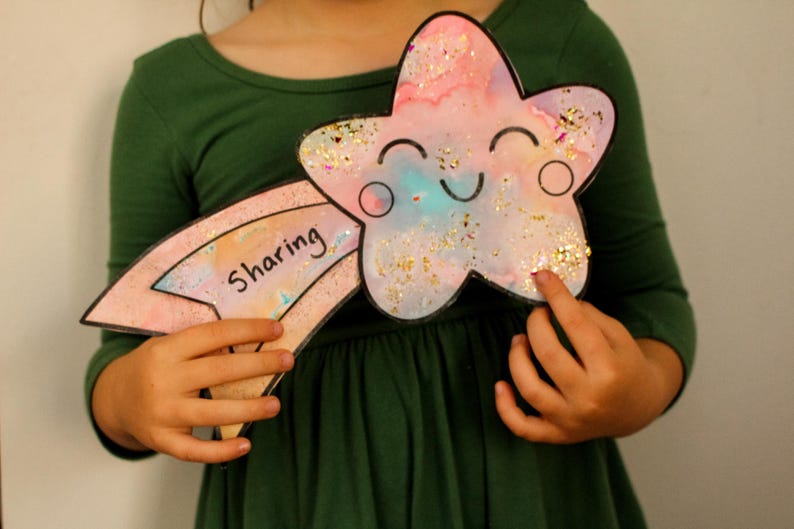 Puede incluir: Un ni&ntilde;o sostiene una estrella rosa y azul con brillantina y una cara sonriente. La estrella est&aacute; unida a un arco&iacute;ris rosa y blanco con la palabra "compartir" escrita en ella.