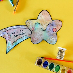 Puede incluir: Una pintura de acuarela de una estrella sonriente con una pancarta que dice "ayudar a alguien". La estrella est&aacute; sobre un fondo amarillo con una paleta de pintura, un pincel y un frasco de purpurina.