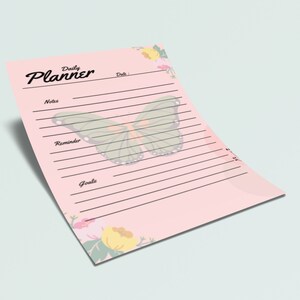 May include: A pink daily planner with a butterfly design and floral accents. The planner has sections for notes, reminders, and goals.