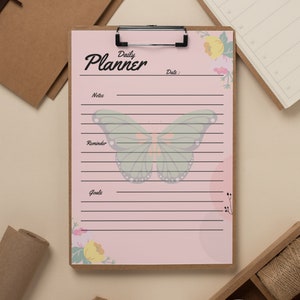 May include: A pink daily planner with a butterfly and floral design. The planner has sections for notes, reminders, and goals.