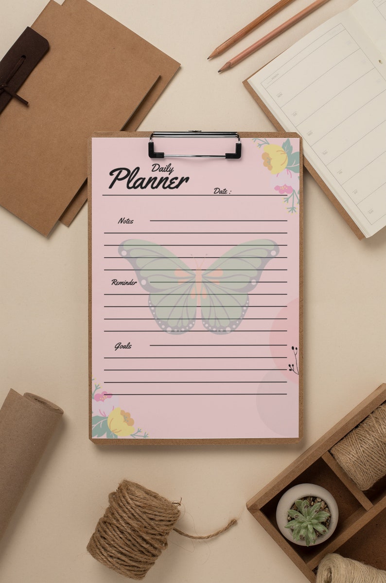 May include: A pink daily planner with a butterfly and floral design. The planner has sections for notes, reminders, and goals.