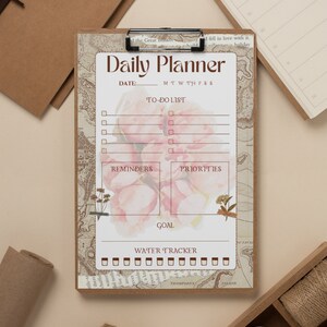 Puede incluir: Un planificador diario con un dise&ntilde;o de mapa vintage y detalles florales. Incluye secciones para listas de tareas, recordatorios, prioridades y un rastreador de objetivos. El planificador tiene un fondo marr&oacute;n con un interior blanco.