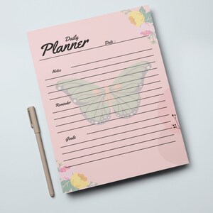 May include: A pink daily planner with a butterfly design and floral accents. The planner has sections for notes, reminders, and goals.