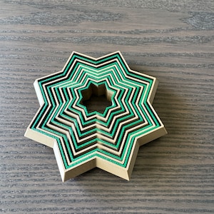 May include: A set of seven nested star-shaped cookie cutters, made of brown plastic with green edges. The cutters are arranged in a circle, with the largest cutter on the outside and the smallest cutter on the inside.