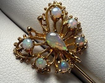 May include: A gold butterfly brooch with six iridescent opal stones. The brooch has a delicate, intricate design and is attached to a gold pin.