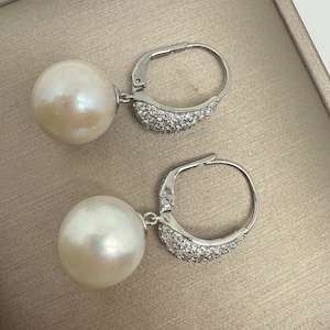 May include: A pair of pearl drop earrings. Each earring has a large, round, white pearl hanging from a silver-tone leverback clasp. The clasp is decorated with small, sparkling crystals, adding a touch of glamour to the jewellery.