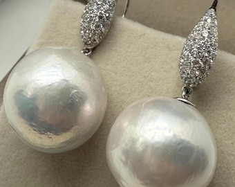 May include: A pair of drop earrings featuring large, round, white pearls suspended from teardrop-shaped silver-toned settings encrusted with numerous small, clear, sparkling stones that catch the light.