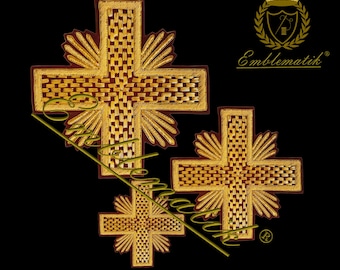 May include: Three gold embroidered crosses on a maroon fabric background. The crosses have a woven pattern and are surrounded by gold fringe. The image includes the text "Emblematik" in a gold font.