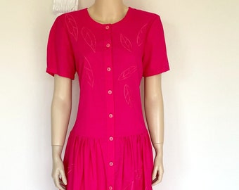 May include: A bright pink dress with short sleeves and a button-down front. The dress features a fitted bodice and a gathered skirt. Delicate leaf-shaped embroidery accents the dress. The dress is displayed on a mannequin.