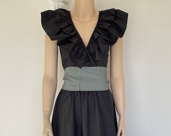 May include: A black midi dress with a ruffled neckline and a gingham belt. The skirt has a tiered ruffle hem.
