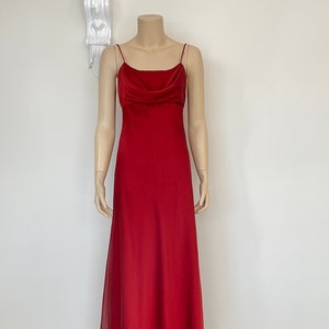 Op de afbeelding: Een lange, rode, mouwloze jurk met een cowl-hals en een zwierige rok.