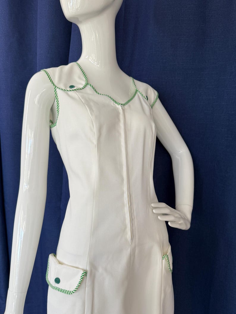 Peut inclure: Robe blanche sans manches avec garniture et d&eacute;tails de poches verts. La robe pr&eacute;sente une encolure ronde et une fermeture &eacute;clair sur le devant. La garniture est un motif de corde verte et blanche. La robe est pr&eacute;sent&eacute;e sur un mannequin.