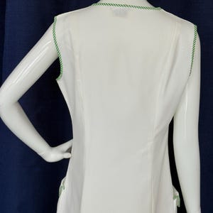 Peut inclure: Robe blanche sans manches avec une bordure verte autour de l'encolure et des emmanchures. La robe pr&eacute;sente un design simple et &eacute;l&eacute;gant, avec une coupe ajust&eacute;e. La bordure verte ajoute une touche de couleur.