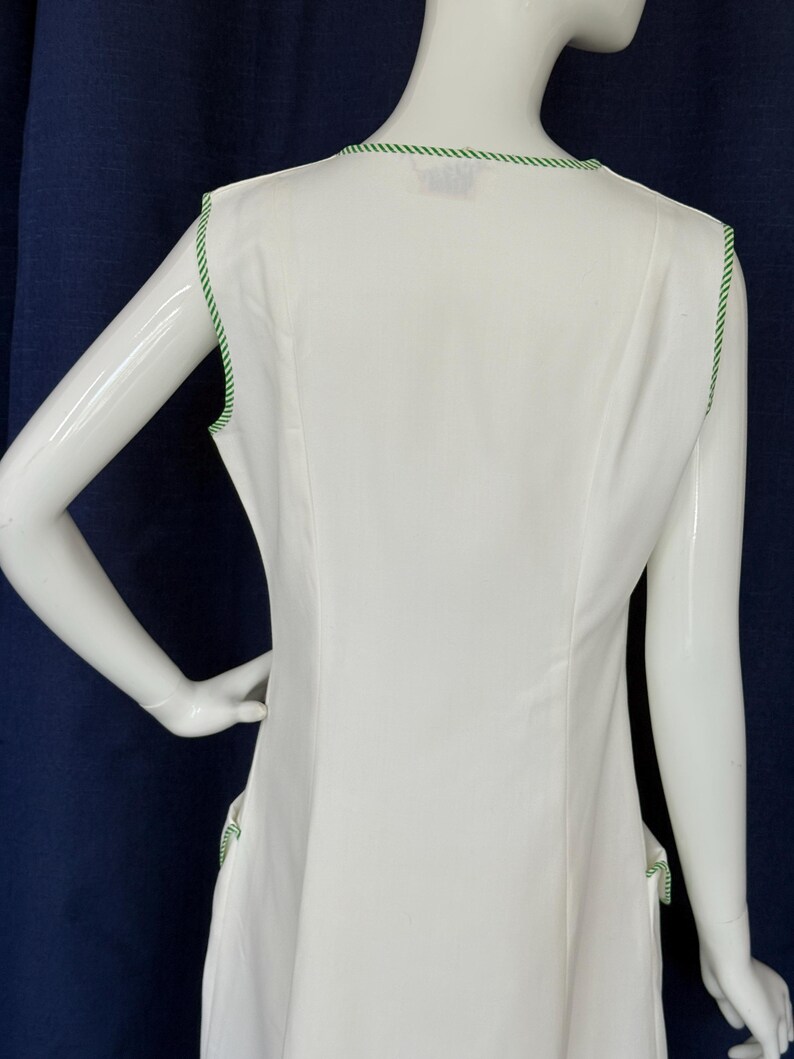 Peut inclure: Robe blanche sans manches avec une bordure verte autour de l'encolure et des emmanchures. La robe pr&eacute;sente un design simple et &eacute;l&eacute;gant, avec une coupe ajust&eacute;e. La bordure verte ajoute une touche de couleur.