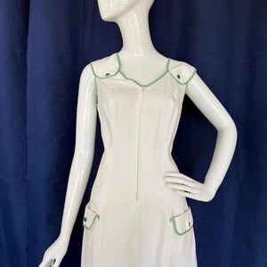 Peut inclure: Une robe blanche sans manches avec des bordures et des accents verts. La robe pr&eacute;sente une encolure en V, une fermeture &eacute;clair sur le devant et deux poches avant. Les bordures et les accents sont de couleur vert vif. La robe est pr&eacute;sent&eacute;e sur un mannequin blanc.