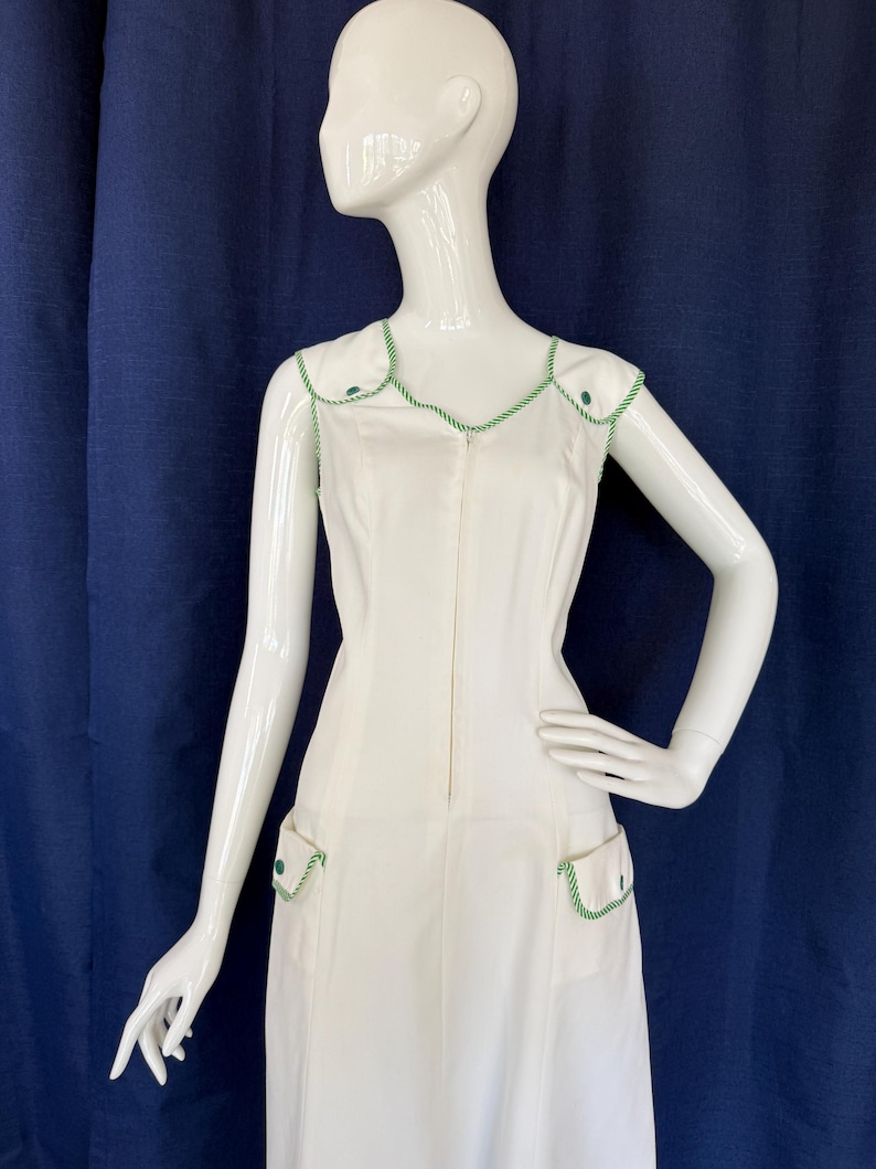 Peut inclure: Une robe blanche sans manches avec des bordures et des accents verts. La robe pr&eacute;sente une encolure en V, une fermeture &eacute;clair sur le devant et deux poches avant. Les bordures et les accents sont de couleur vert vif. La robe est pr&eacute;sent&eacute;e sur un mannequin blanc.