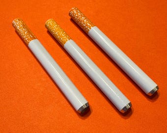 May include: Three white and orange cigarette-shaped objects with silver tips are arranged diagonally on an orange surface. The ends of the objects are orange with white speckles, and the bodies are white.