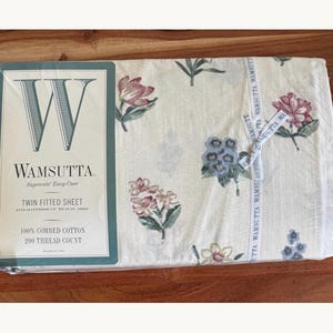 May include: A Wamsutta twin fitted sheet in a cream color with a floral pattern featuring pink, red, and blue flowers. The packaging includes the text Wamsutta, Supercale Easy-Care, Twin Fitted Sheet, 100% Combed Cotton, and 200 Thread Count.