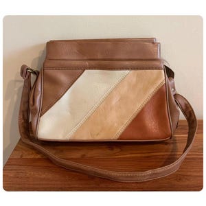 May include: A rectangular shoulder bag featuring a multi-toned design with diagonal stripes in shades of cream, light tan, and dark brown. The bag includes a matching brown shoulder strap, a top flap closure, and visible stitching along the panels.