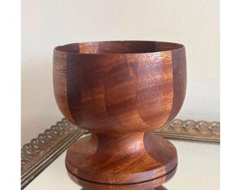 May include: A wooden bowl with a pedestal base. The bowl is made of dark wood with a natural grain pattern. The bowl is round and has a wide opening.