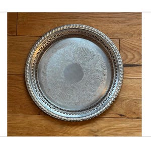 May include: A silver serving tray with a decorative embossed design. The tray has a scalloped edge and a rope-like border.