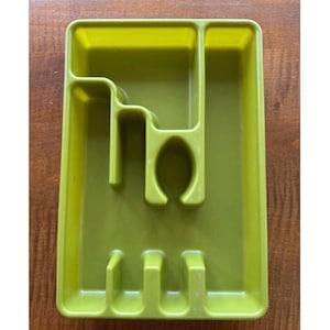 May include: A green plastic cutlery tray with multiple compartments for organizing silverware. The tray has a rectangular shape with various slots and dividers to separate forks, knives, and spoons. The tray is set on a wooden surface.