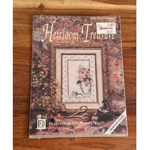 May include: A cross-stitch kit titled "Heirloom Treasure" featuring a floral design. The kit includes a framed image of a vase with pink flowers. The package dimensions are 5 x 7 inches (12.7cm x 17.78cm).