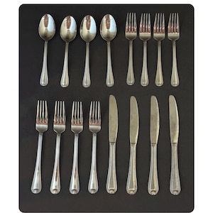 May include: A collection of silver-colored flatware, including spoons, forks, and knives, arranged on a dark surface. The spoons are oval-bowled, and the forks and knives have a simple, elegant design. This set is ideal for formal dining.