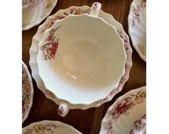 Pode incluir: Um conjunto de chávenas de chá e pires vintage com um padrão floral em tons de rosa, vermelho e amarelo. As chávenas e os pires têm uma borda ondulada e são feitos de porcelana branca.