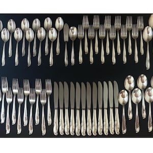 May include: Arrangement of silver-colored flatware, including spoons, forks, and knives, on a black surface. The utensils are neatly organized, showcasing a complete set for dining. The silverware has a reflective surface.