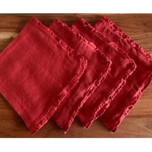 May include: Four red linen napkins with a ruffled edge are arranged on a wooden surface. The napkins are square and have a slightly textured appearance. The color is a vibrant, solid red.