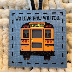 May include: A blue and black wooden sign with the text "We love how you roll" and a yellow school bus cutout. The bus has the words "School Bus" on the front.