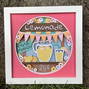 May include: A framed paper craft depicting a lemonade stand with a pitcher of lemonade, lemons, a glass of lemonade, and a sign that says "Fresh Squeezed". The stand is decorated with flowers and flags. The price is 25 cents.