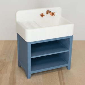 May include: A white porcelain sink with a copper faucet mounted on a blue wooden cabinet with two shelves.