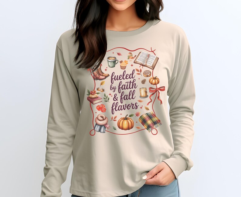May include: A beige long-sleeve shirt featuring a central graphic with the text "fueled by faith & fall flavors" surrounded by illustrations of a coffee mug, an open book, a pumpkin, a candle, a plaid blanket, boots, and autumn leaves.