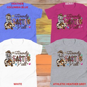 May include: Four different color t-shirts featuring a cartoon bunny wearing a cowboy hat and holding an Easter egg. The text on the shirts reads "Howdy Easter Y'all". The t-shirt colors are heather columbia blue, berry, white, and athletic heather grey.