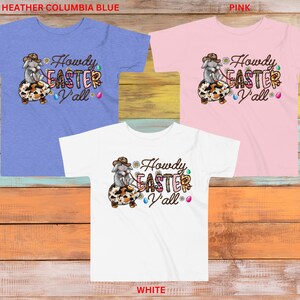 May include: Three t-shirts with a graphic of a cartoon bunny wearing a cowboy hat and riding an Easter egg. The text "Howdy Easter Y'all" is on the shirts. The shirts are in heather columbia blue, pink, and white.