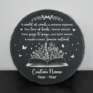 May include: Round black slate plaque with white text and illustrations. The text reads "A world of words...forever restored." An open book illustration is at the bottom, with butterflies and floral designs. The words "Custom Name" and "Year - Year" are also present.