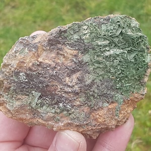 Puede incluir: Primer plano de una roca con un patrón en capas verde y marrón. La roca tiene una textura rugosa y está cubierta de pequeños cristales.