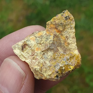 May include: A close-up of a yellow and orange rock with a rough texture. The rock is being held in a hand.