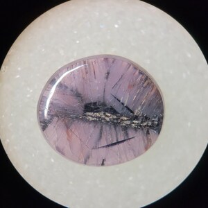 May include: A close-up of a purple and black gemstone with a white background. The gemstone has a unique pattern of lines and swirls.