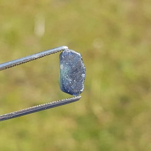 以下が含まれることがあります： ぼやけた緑色の背景にピンセットで保持された濃い青色の宝石