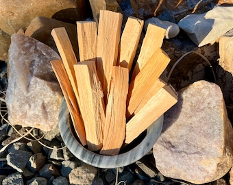 May include: A close-up of a gray bowl filled with bundles of dried Palo Santo wood sticks. The sticks are light brown and have a natural, rough texture.