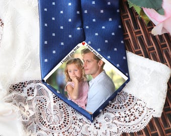 May include: Navy blue tie with a white square pattern. A photo of a man and a child is centered on the tie, with the text "I loved you first" and "I love you dad". The tie is displayed on a white lace surface.