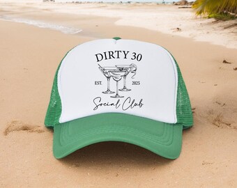 May include: A green and white trucker hat with the text "DIRTY 30 Social Club" and a graphic of three martini glasses. The hat has a curved brim and a mesh back, perfect for a casual look.