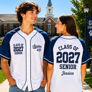 Puede incluir: Una camiseta de béisbol blanca y azul marino con el texto Class of 2027 Senior en el frente y la espalda. El frente incluye el nombre Austin y el número 27, mientras que la espalda muestra el nombre Jessica en cursiva bajo el texto.